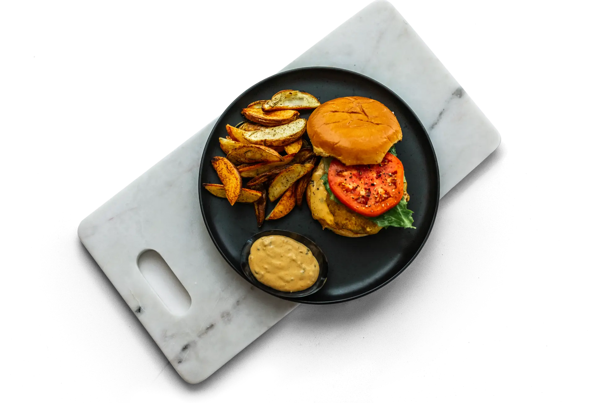 Plated burger with potato wedges and dipping sauce on a marble board