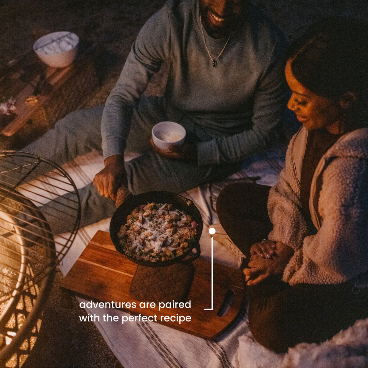 Couple sharing a skillet meal by the fire — adventures paired with the perfect recipe