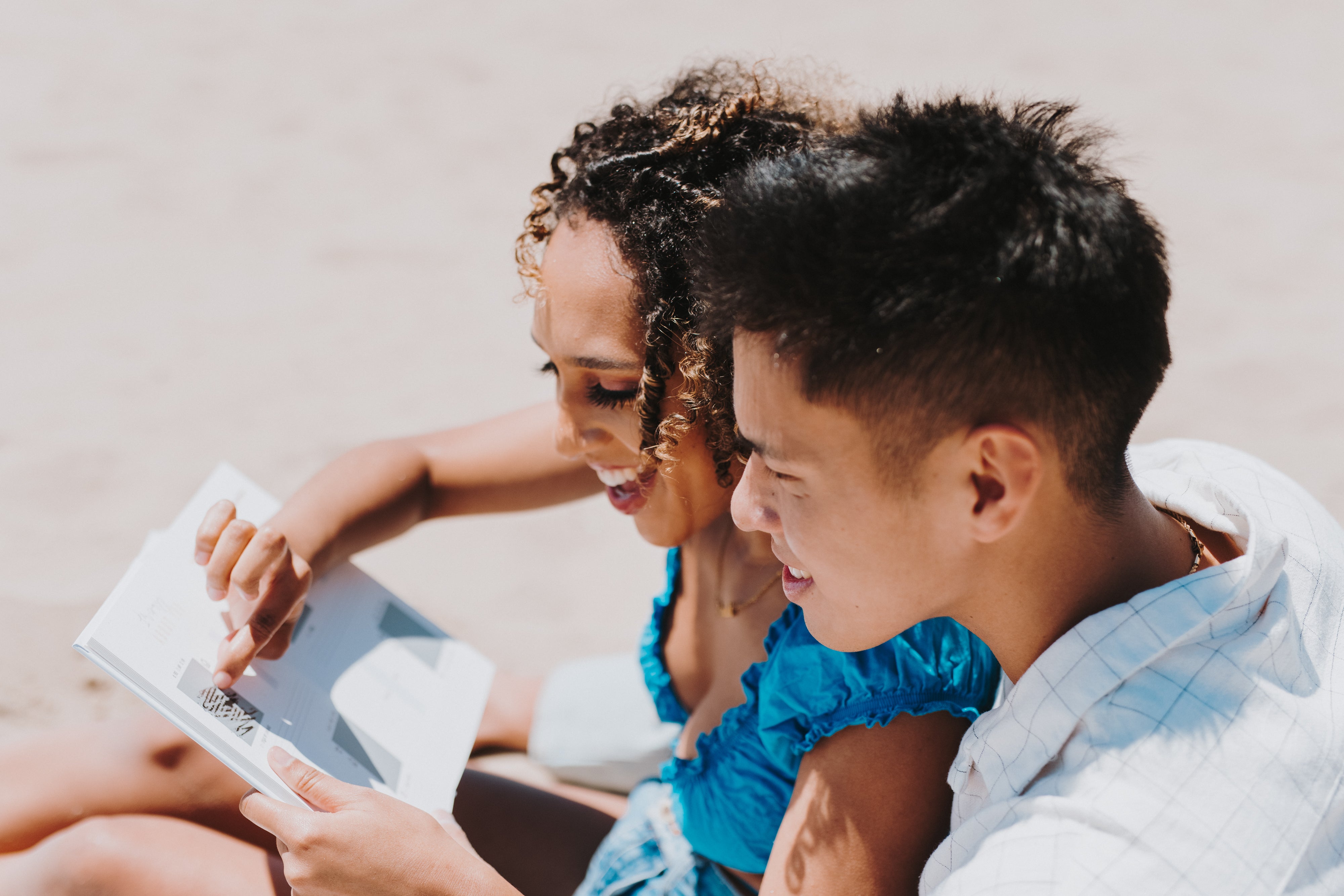 Couple sitting together on the sand as they read The Adventure Challenge: Couples Edition