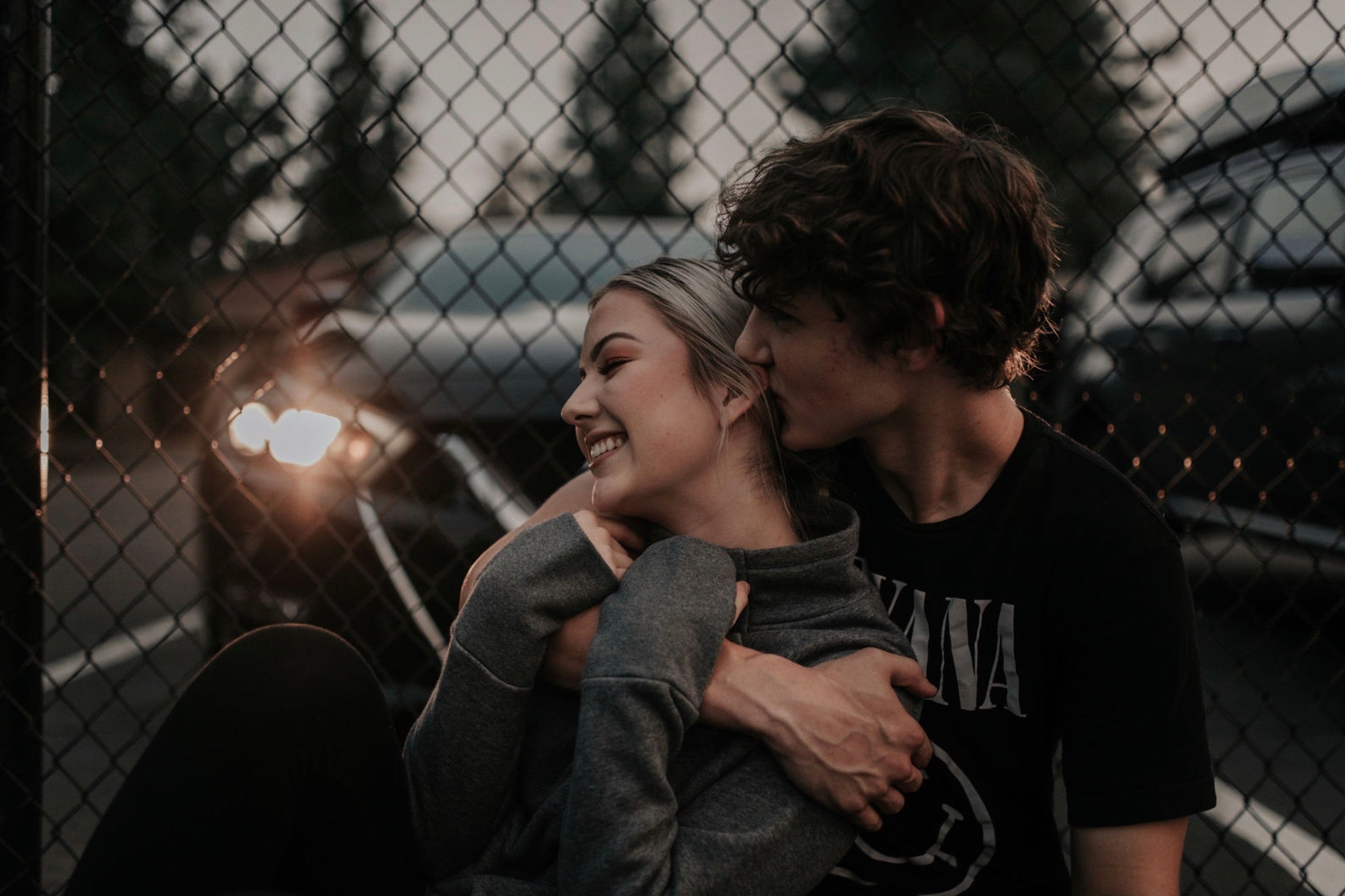 10 Ways on How To Be a Better Lover: Couple sharing an embrace in front of their car behind fence.