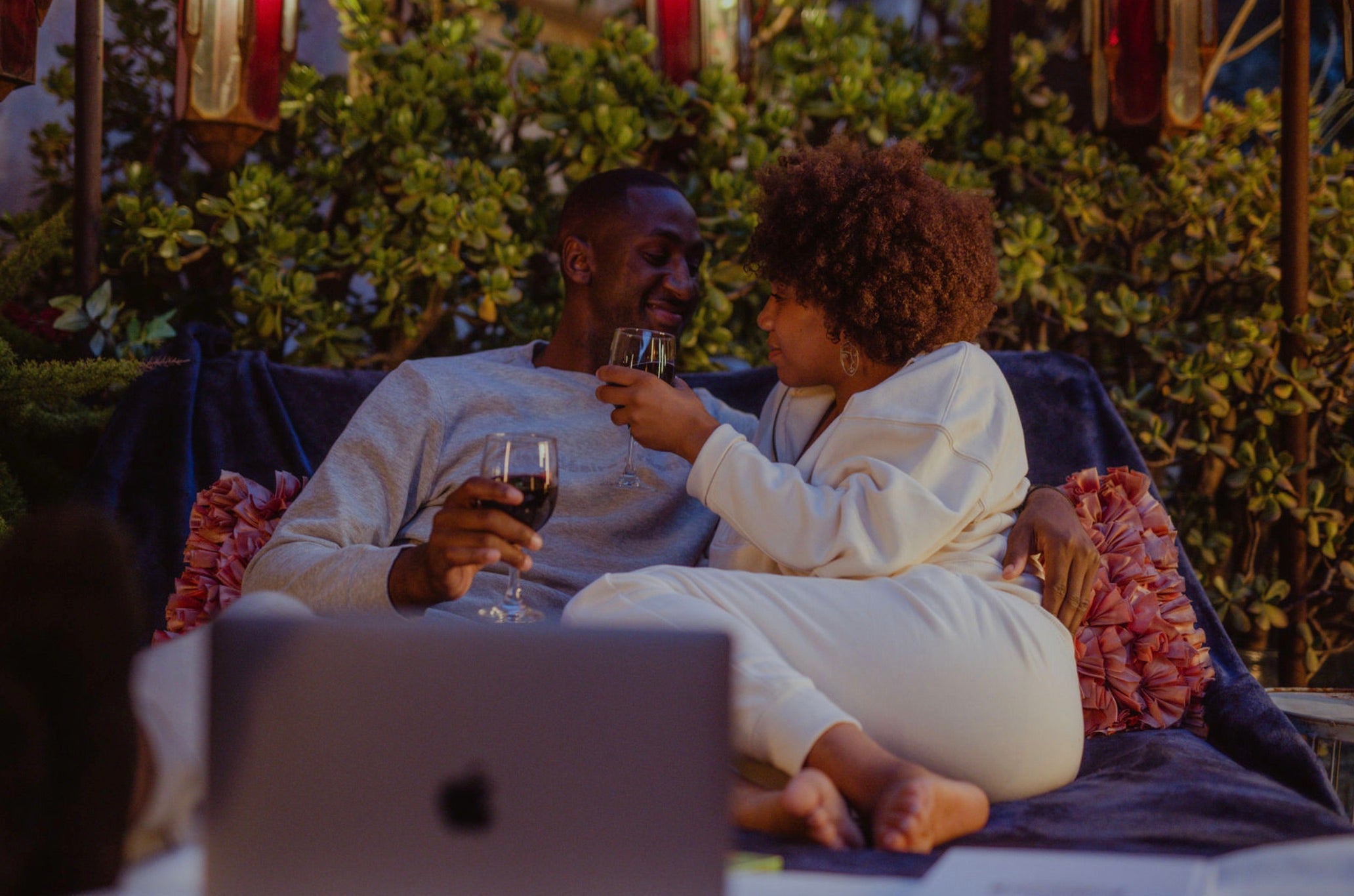 Couple smile at each other as they snuggle and enjoy a glass of wine together
