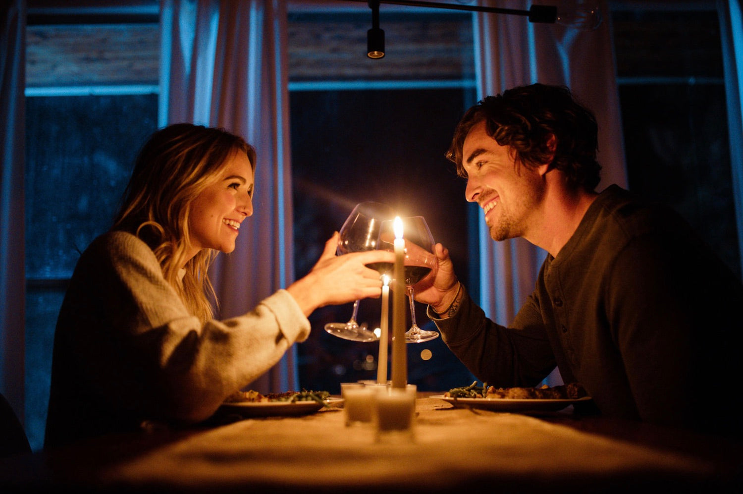 Couple smiling at each other as they share a toast during their romantic candlelit dinner together