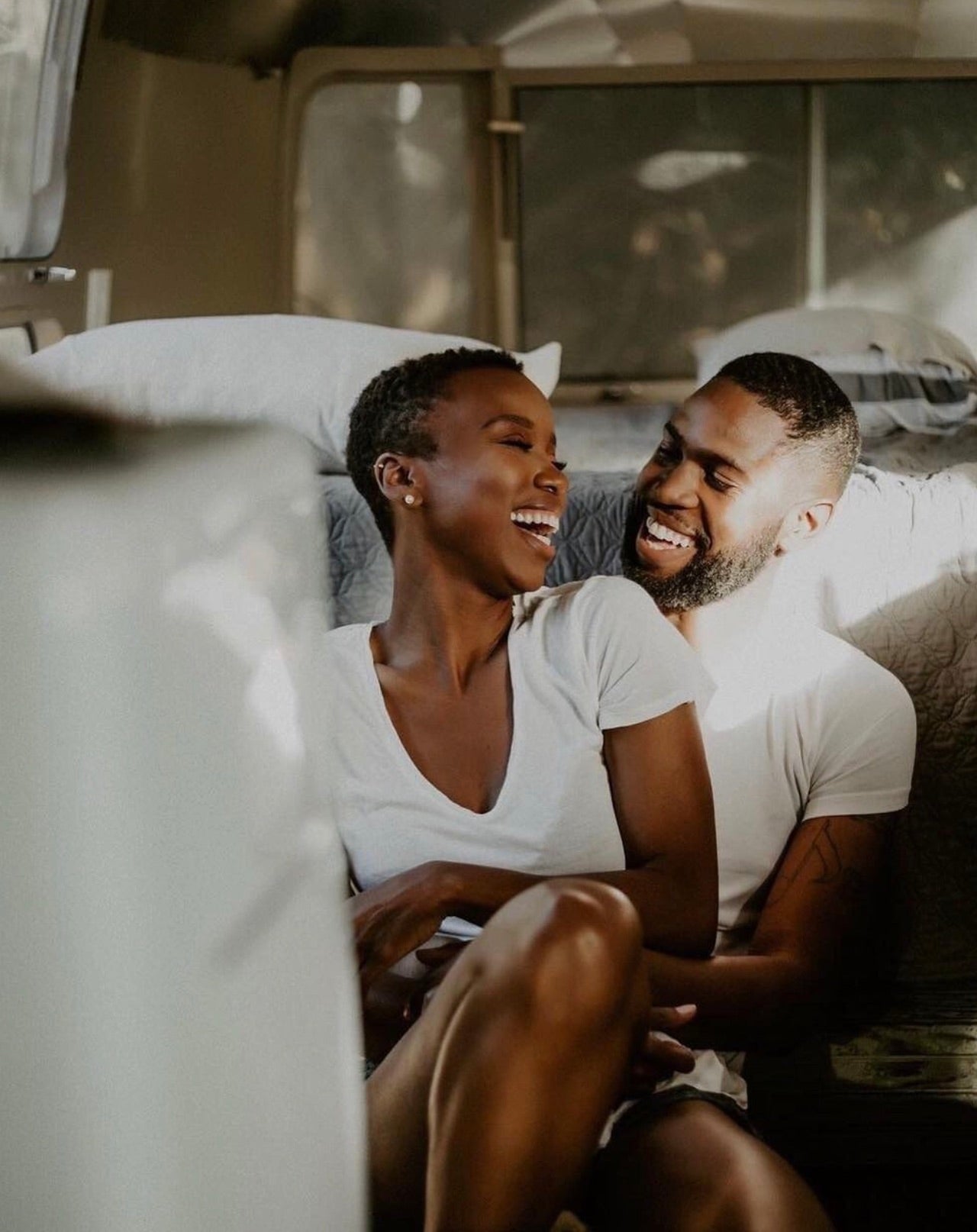 Couple laughing as they sit close to each other with the sunlight shining on them