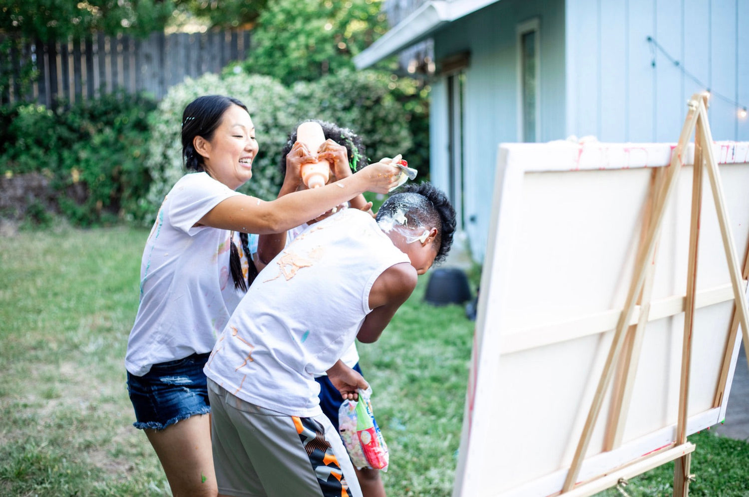 29 Fun Activities To Do At Home With The Kids. Mother and her two sons playing with paint in their own backyard.