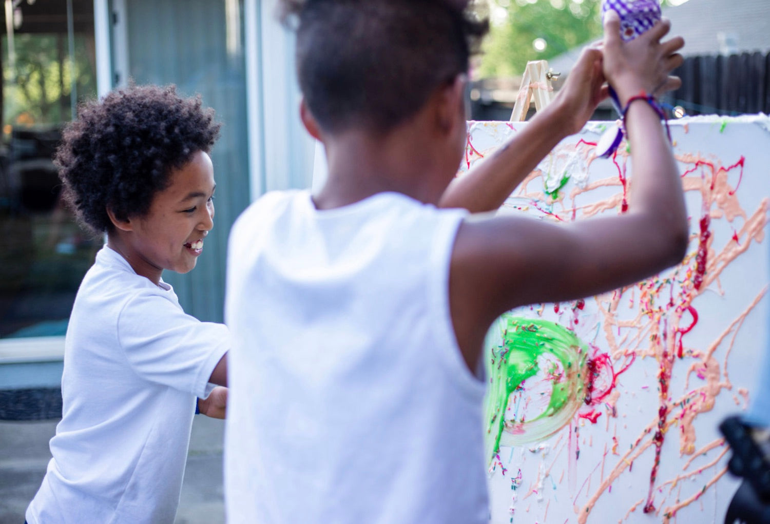 Two little boys having fun squeezing paint onto a white canvas