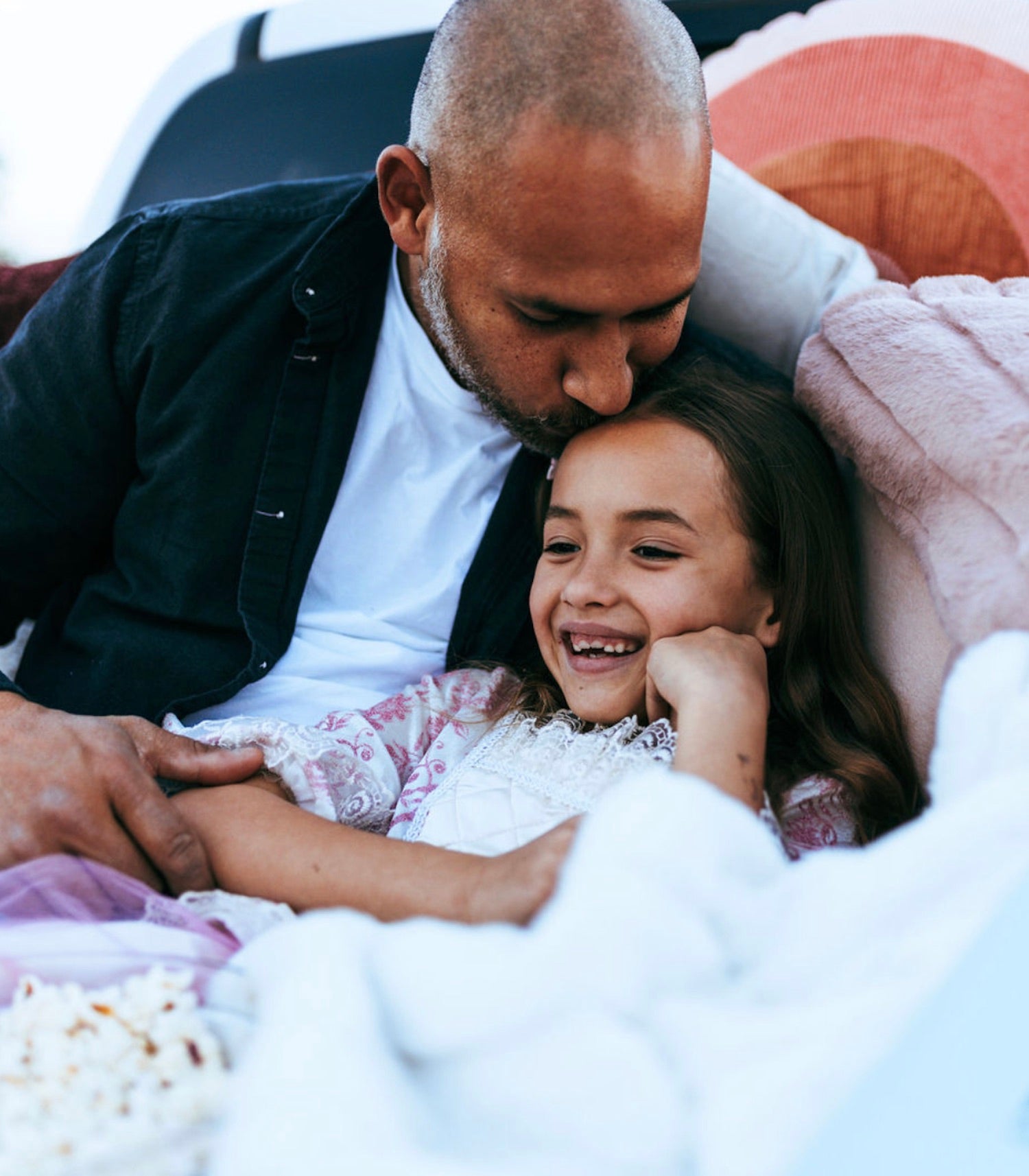 13 calming bedtime activities for a more peaceful sleep for your children: Father planting a kiss on his daughter's forehead as she smiles while they both sit on a couch