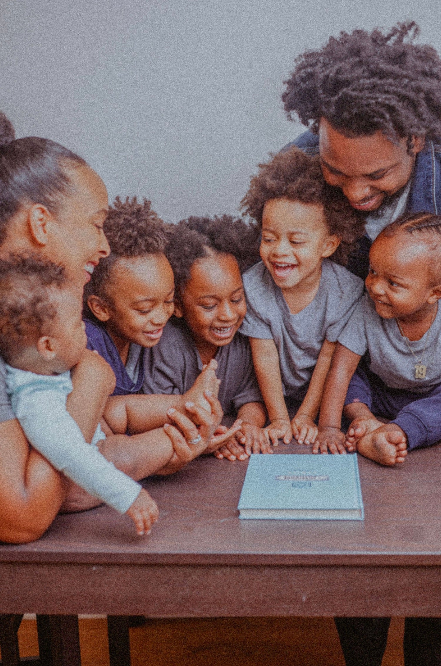 Family of seven smile and gather around a table with a copy of The Adventure Challenge: Family Edition on top.