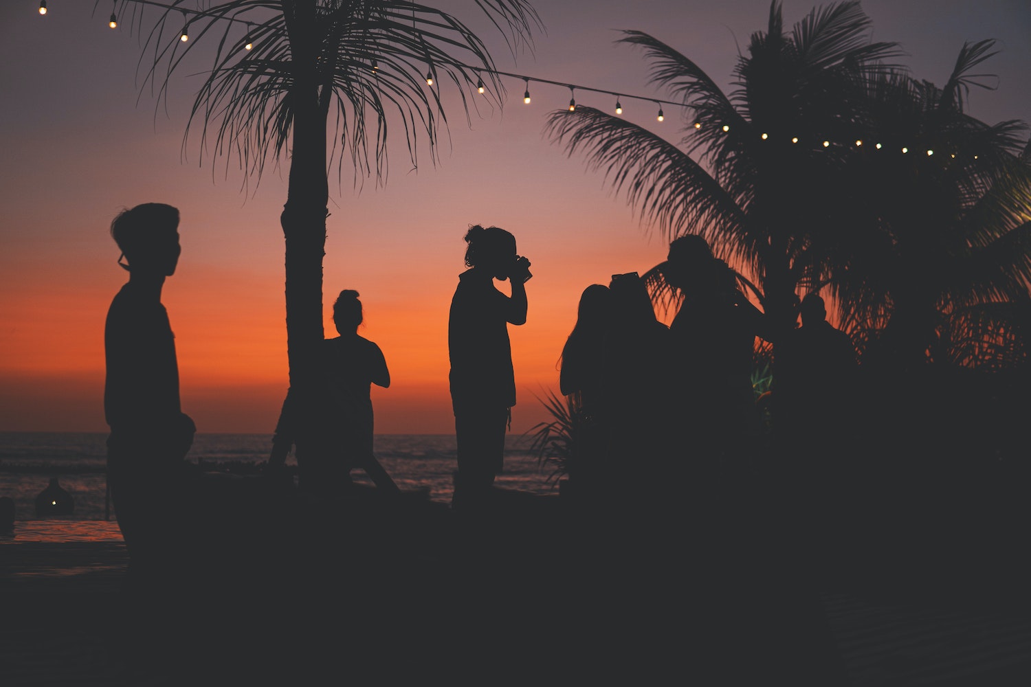 Fun Things To Do With Friends (Summer 2021). Silhouette of a group of friends having drinks at the beach.