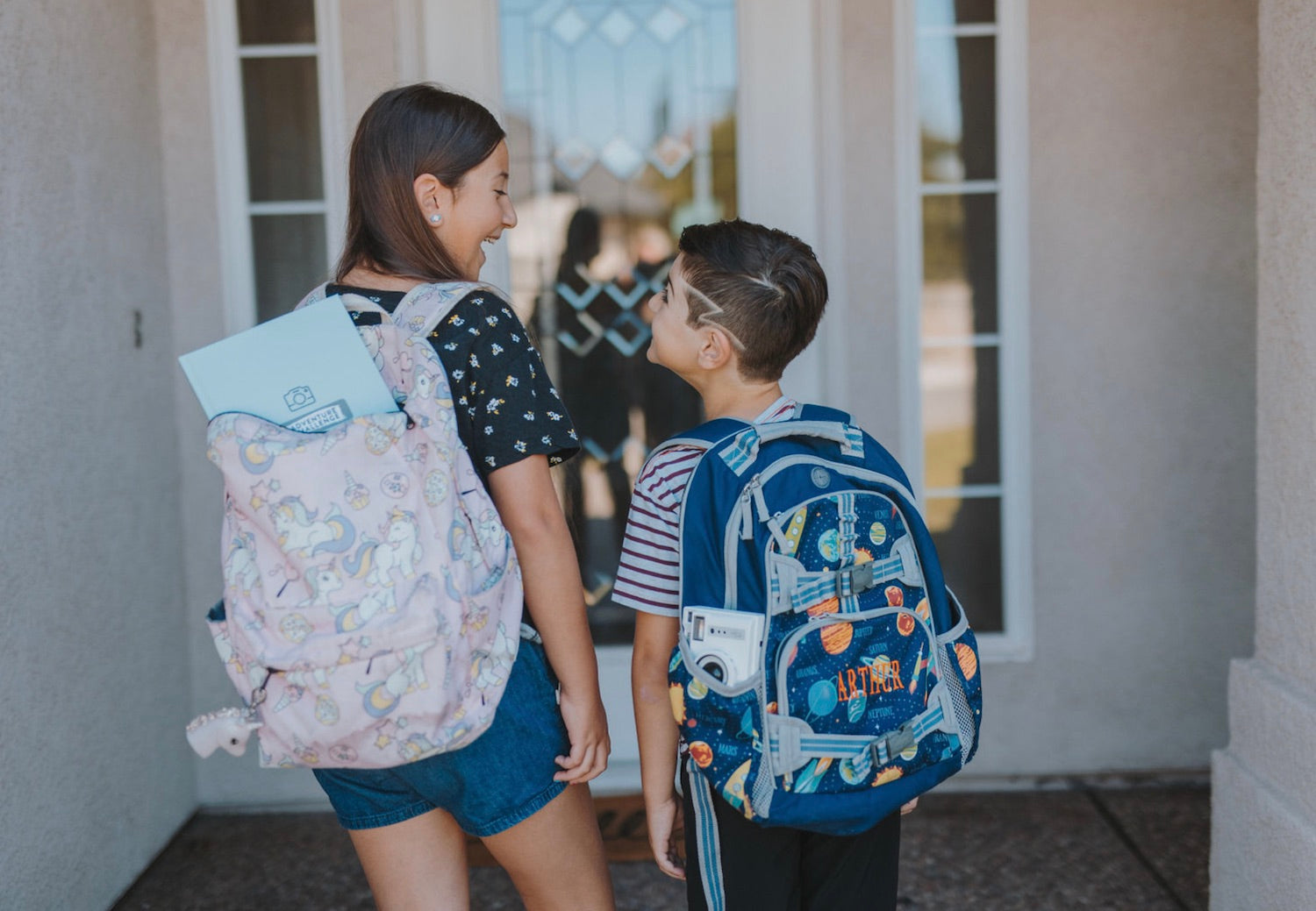 ​​How to Get the Best Deals on Back to School Supplies. Boy and girl smile at each other while carrying their backpacks home after a day in school.