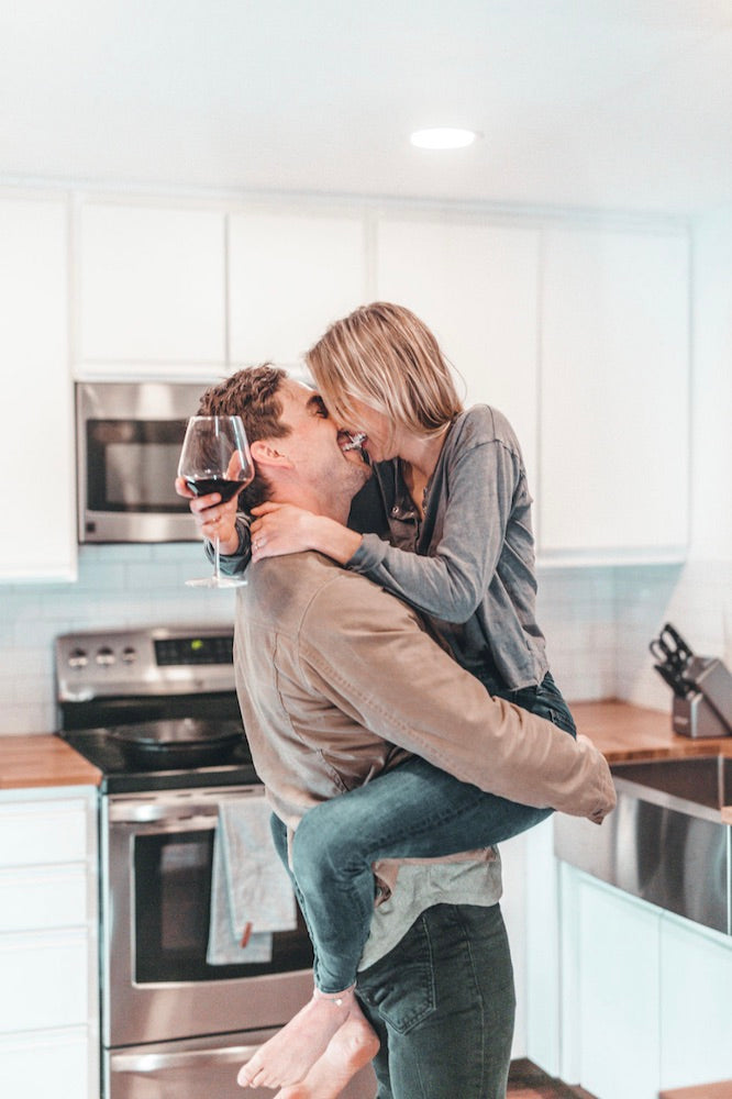 How to Spice Things Up in The Bedroom in 2021. Boyfriend carries girlfriend in his arms as they share a laugh in the kitchen.
