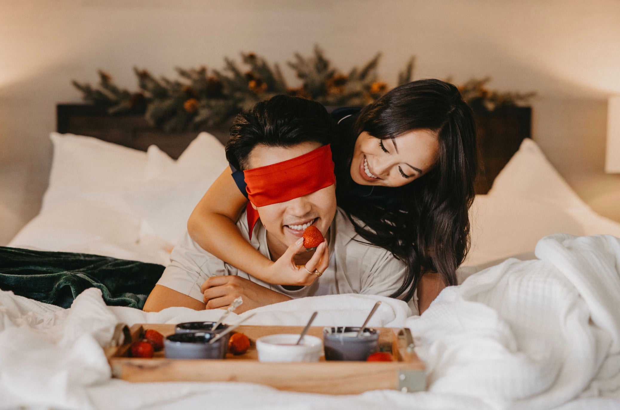 Wife feeds husband strawberries as he is blindfolded in bed
