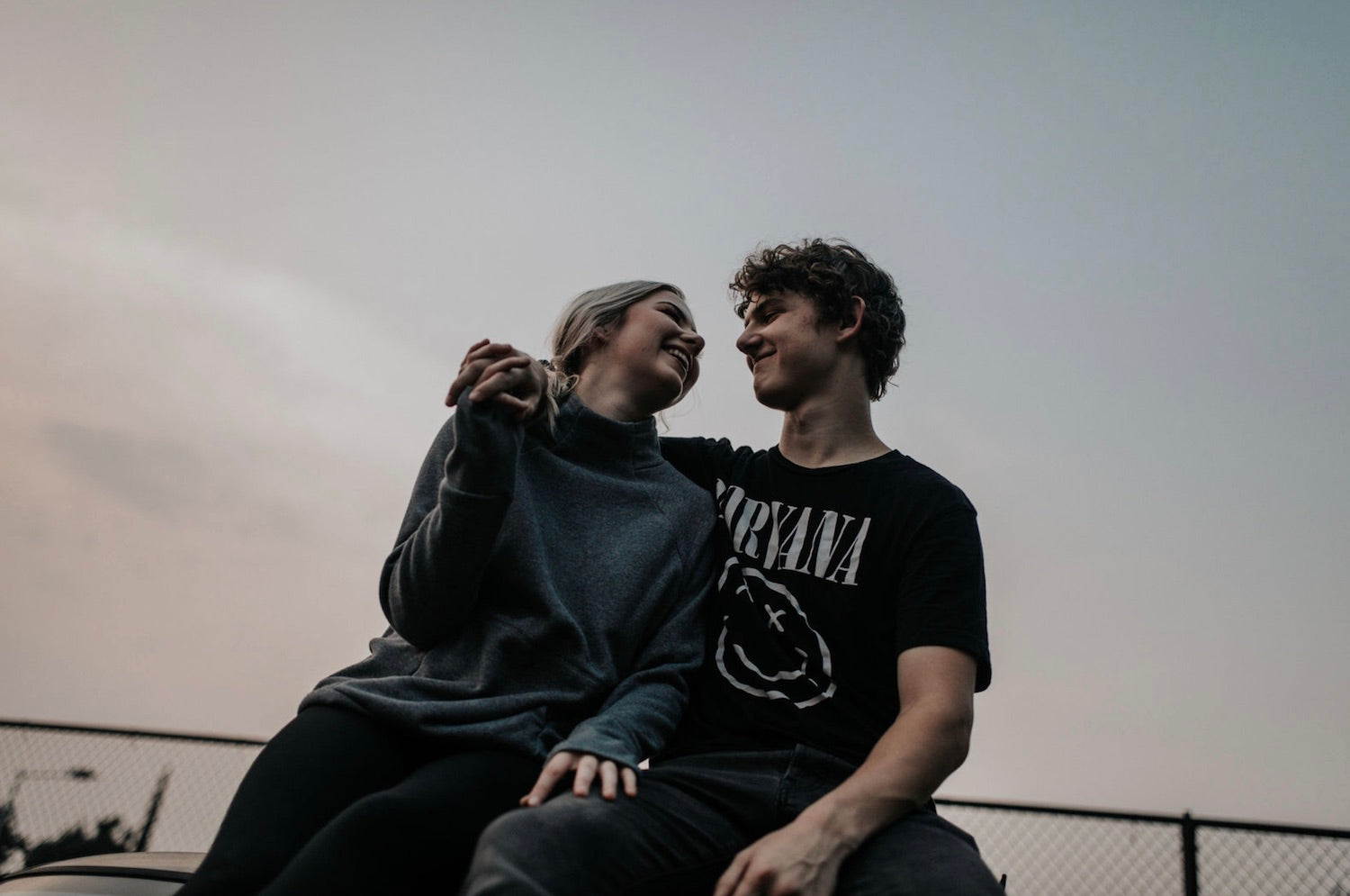 A couple smile at each other as they sit on bleachers at twilight