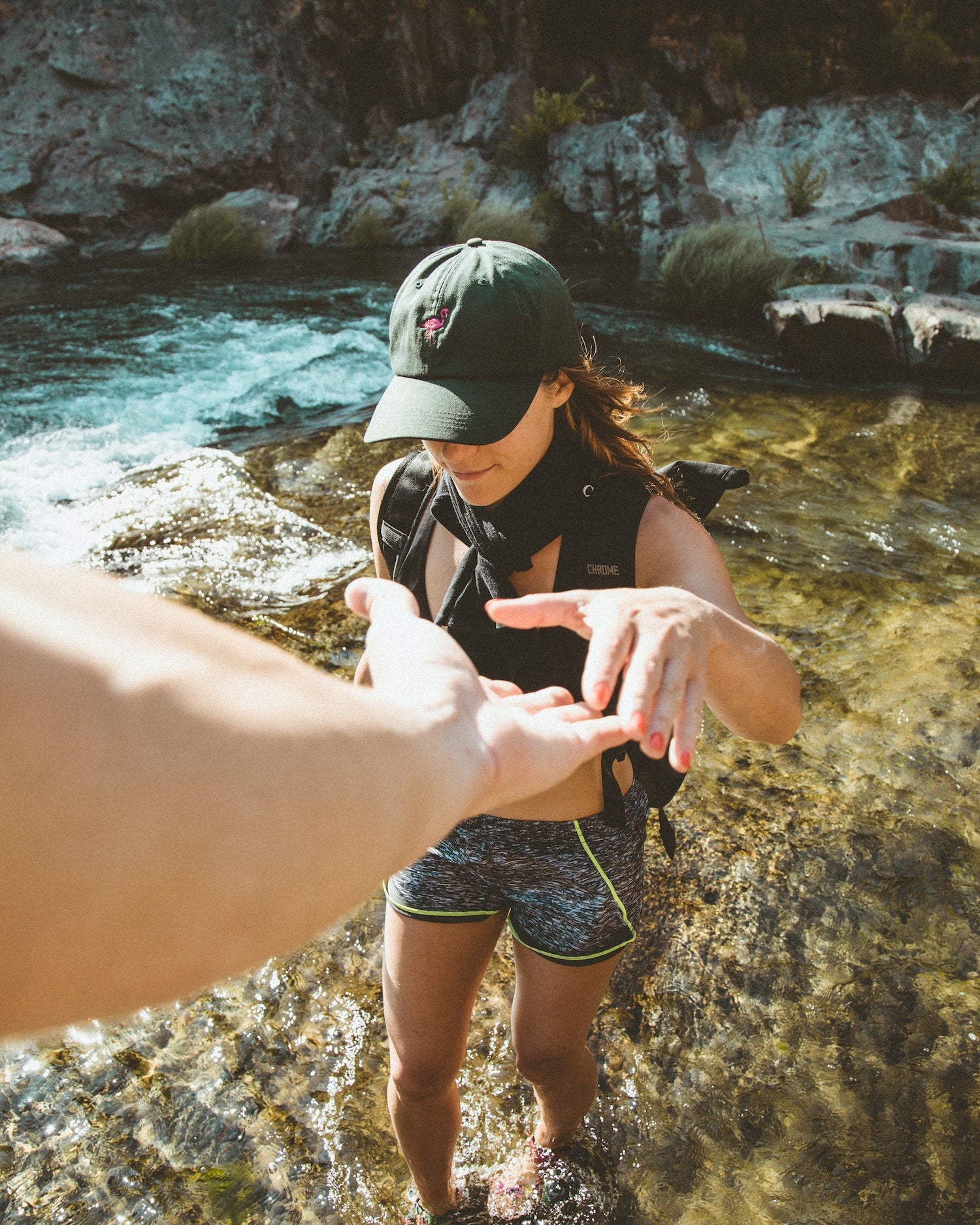 A man reaches out his hand to help his girlfriend as they hike up a cliffside together and she reaches for his hand