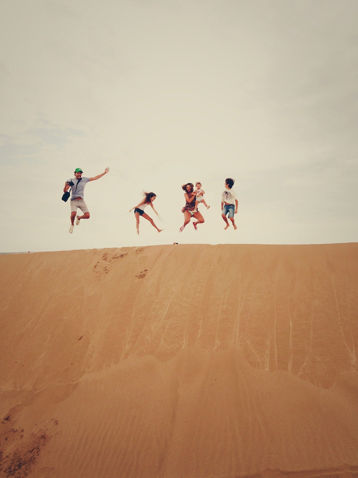 Plan a Family Adventure That Your Kids Won't Stop Talking About. Family posing for a jump shot at the sand dunes