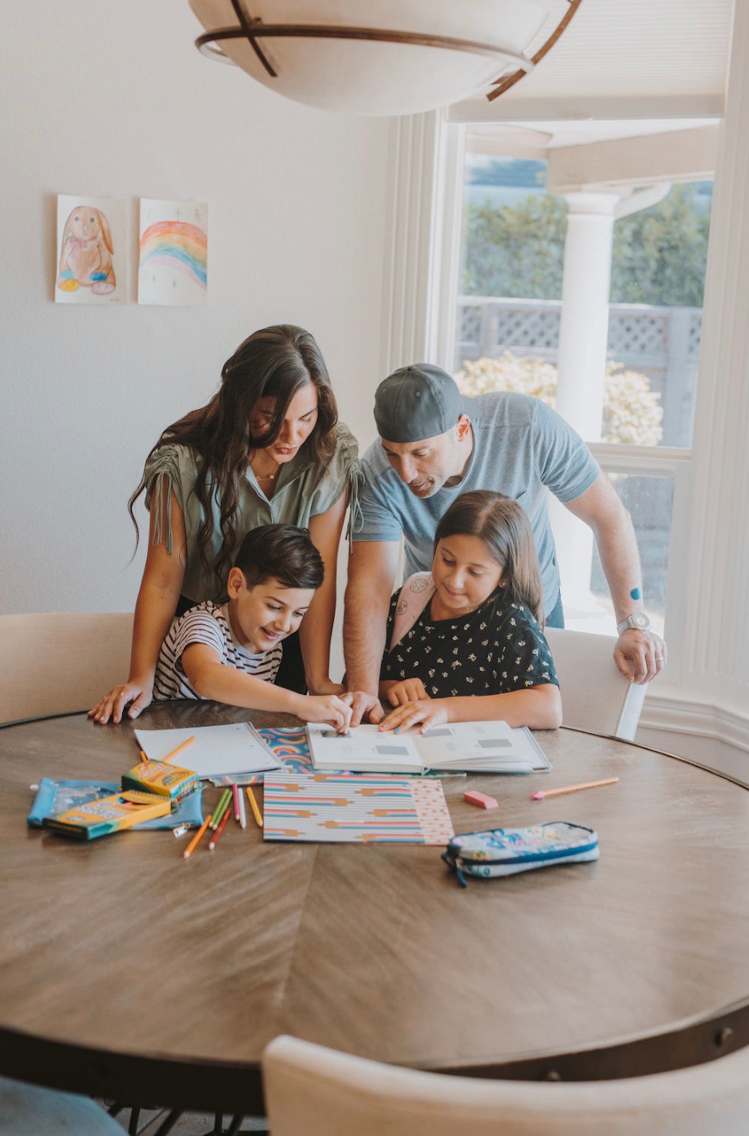 The Ultimate Back to School List for 2021. Mom and dad hover over their two kids as they do their homework for school.