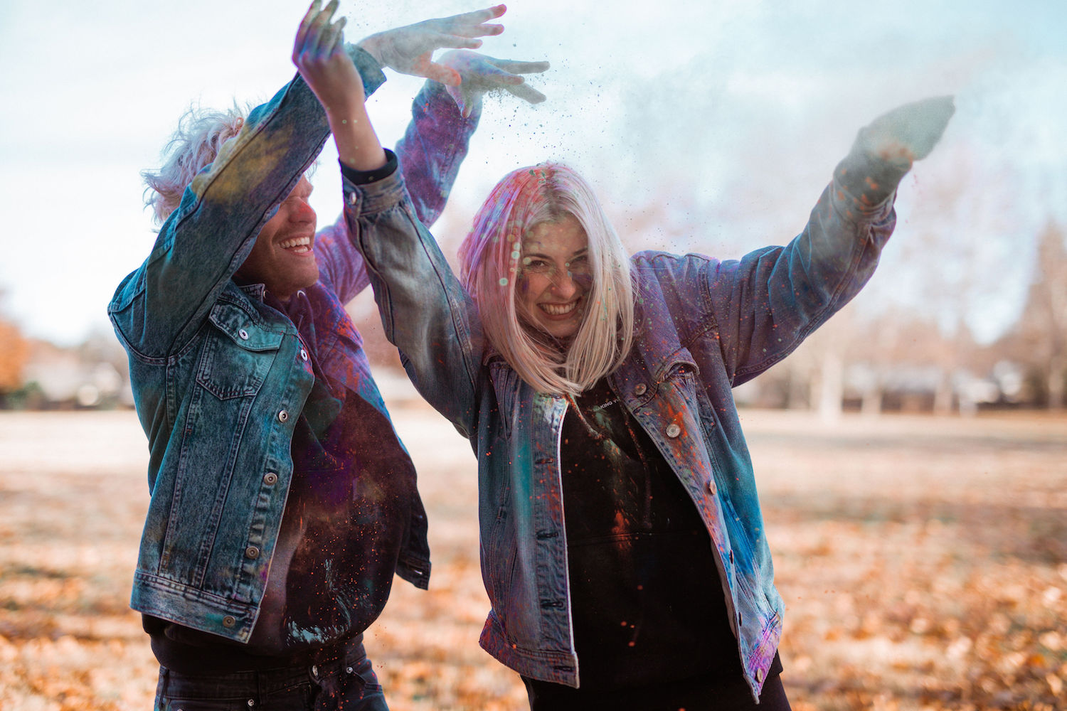 Two friends smile while throwing colored powder in the air